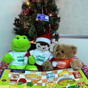 Sheldon the elf sitting by a Christmas tree with a Pollywog frog and a Vroom bear reading a book