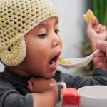 A toddler infected by the flu virus is being spoon fed some homemade soup by his dad.