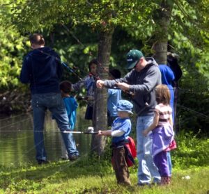 圖為父母和孩子在綠草如茵的河岸上釣魚。